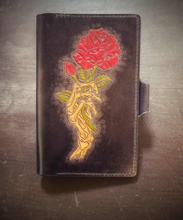 Notebook with 2 roses in a skeleton hand on a black background