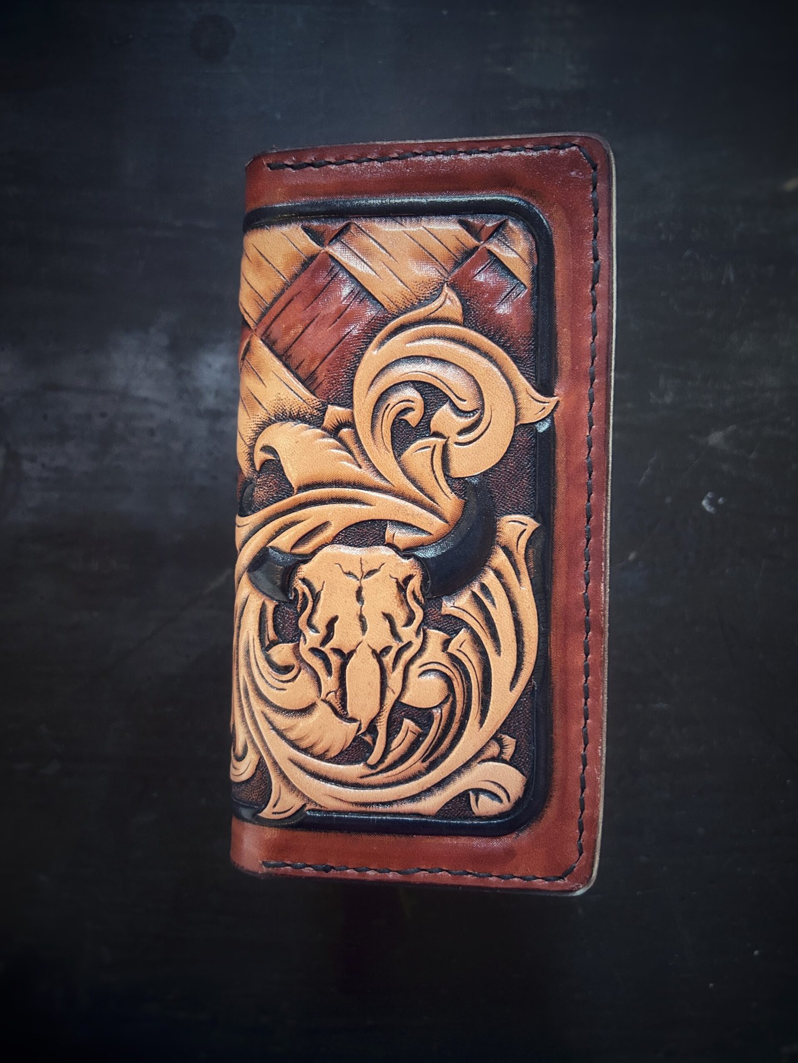 Boulder wallet exterior, brown and tan basketweave background and black boarder. Western scroll and cow skull in lower right corner.