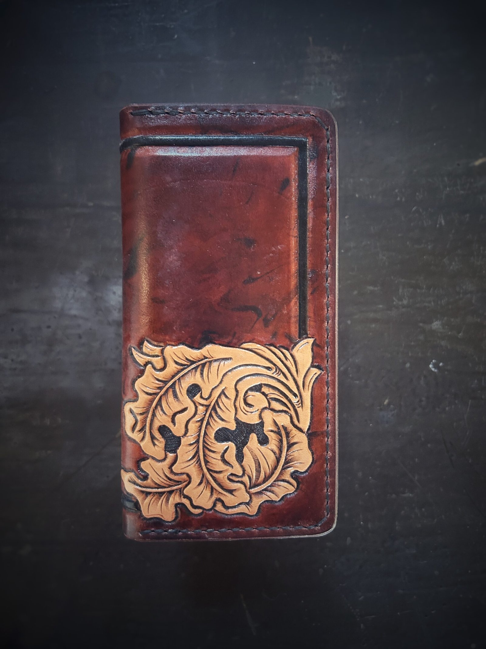 Boulder wallet exterior, brown and black marbled background with black boarder and oak leaves in lower right corner
